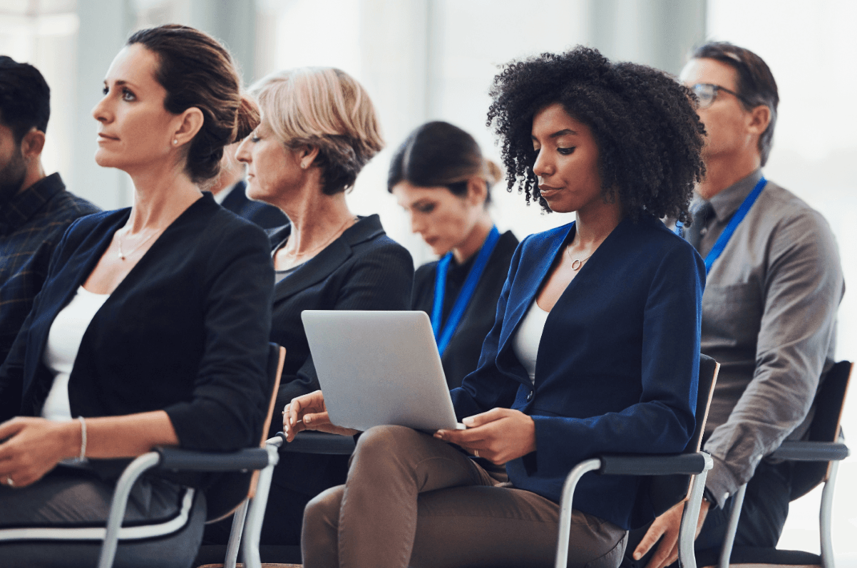 Black woman sitting with a computer on her lap with other people seated in rows.
